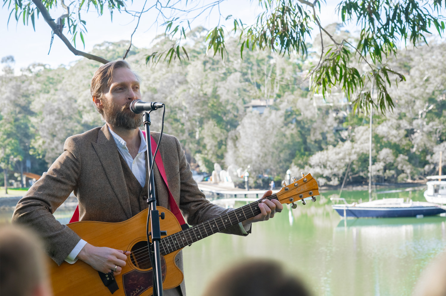 Robert Rosina singing into a microphone with acoustic guitar beside the water